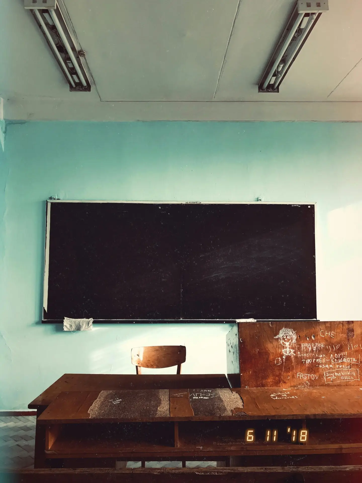 Interior of shabby school classroom with teacher desk and empty blackboard on blue wall